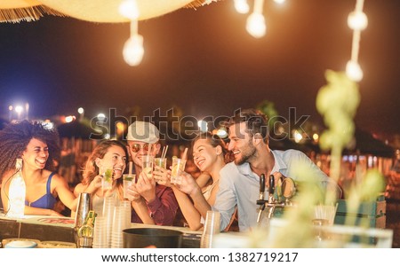 Happy friends cheering and drinking cocktails at beach party outdoor - Young millennials people having fun at weekend summer night - Youth lifestyle and nightlife concept - Main focus on right guys Royalty-Free Stock Photo #1382719217