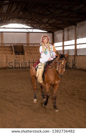 girl in clothes and a headdress of a native americans riding a horse in a pen in an arena