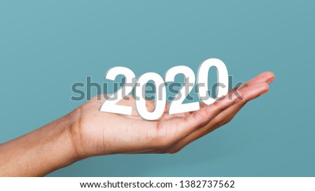 White 2020 year numbers in woman's hand at blue background. 2020 year trends concept. Royalty-Free Stock Photo #1382737562