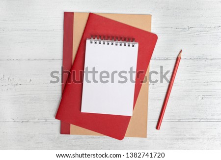 Stack of notebooks and a red pencil on a white wood background. Flat lay with copy space