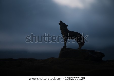 Silhouette of howling wolf against dark toned foggy background. Halloween horror concept. Artwork decoration. Selective focus