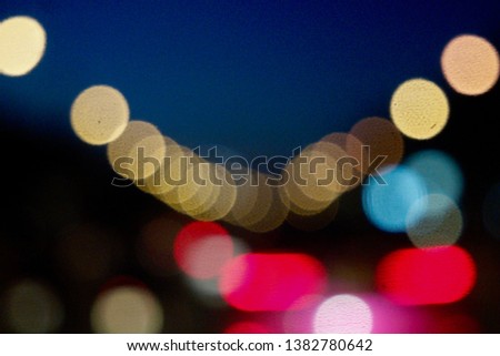 Blurred abstract, colorful bokeh lighting of traffic light in the city at night time on car windshield view, dark tone, selective focus.