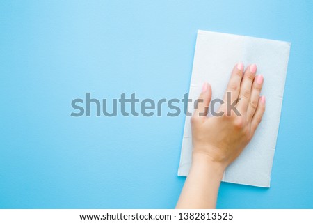 Woman's hand wiping pastel blue desk with white paper napkin. General or regular cleanup. Close up. Empty place for text or logo. Royalty-Free Stock Photo #1382813525