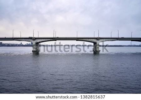Cloudy cityscape of Dnipro with bridges through Dnieper river on the sky background in Ukraine. There are moving cars and a bicyclists on the nearest bridge. Aerial horizontal photo.