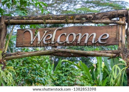 Text welcome on a wooden board in a rainforest jungle of tropical Bali island, Indonesia. Welcome wooden sign inscription in the asian tropics, close up