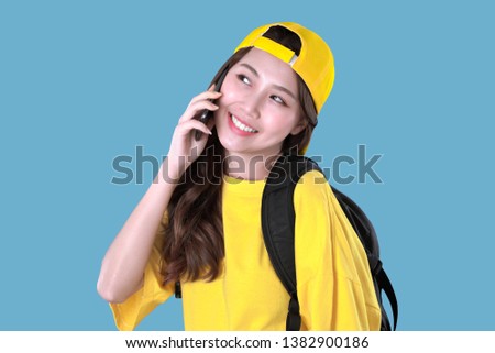 Korean woman backpacker recommended to use apps on smartphone, yellow t-shirt clothing with cap, blue background