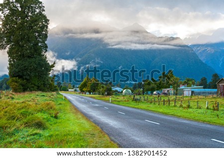 Foggy asphalt empty road to Fox Glacier Village with mountains on the horizon, New Zealand 