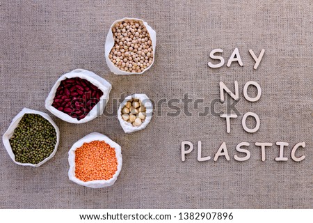 Reusable shopping bags on background of burlap. Wooden letters with inscription say no to plastic. Pouches with 
chickpeas, hazelnuts, green and purple beans, lentils. Zero waste concept.