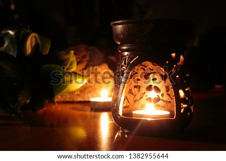 Wax warmer, wax melt, warmer candle with candle light inside. Picture was took with natural light from the fire. In the background are stone and plant.