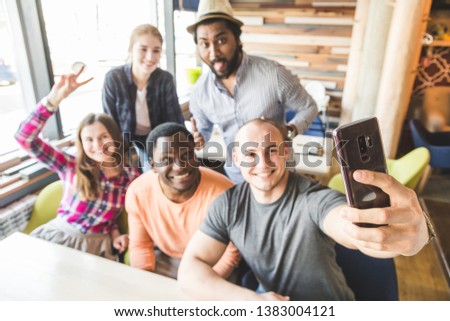Group of young cheerful friends are sitting in a cafe, eating, drinking drinks. Friends take selfies and take pictures.