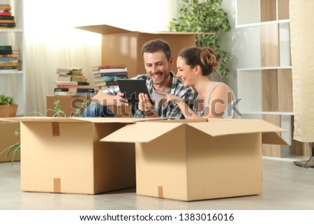 Happy couple moving home checking tablet content sitting on the floor