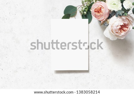 Feminine wedding, birthday mock-up scene. Blank paper greeting card. Bouquet of blush pink English roses, ranunculus flowers and eucalyptus leaves. Concrete table background. Flat lay, top view.