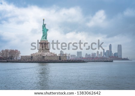 Statue of Liberty and Liberty Island under a dramatic sky, looking out on Ellis Island with the city skyline