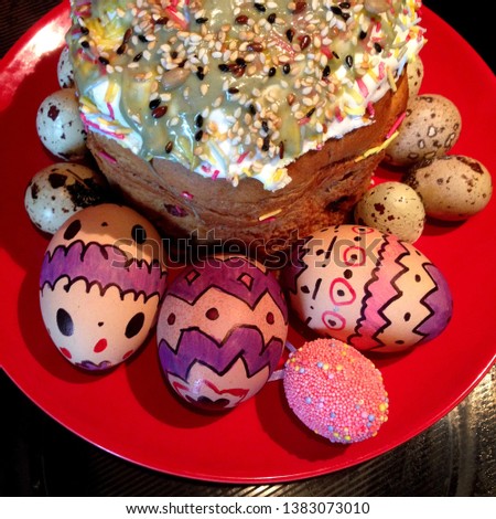 Macro Photo of festive food Easter cake and painted eggs. Easter bread decorated with sesame and seeds. Eggs are boiled and painted with patterns and drawings. Easter bread and eggs on a red plate.