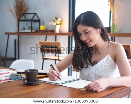 indoor picture of smiling Asia woman writing with notebook