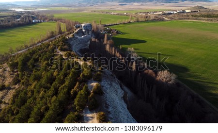 Top view of green fields and rock wall. Shot. Panoramic view of natural stone wall with trees on background of houses and mountain horizons on sunny summer day
