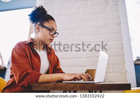 Side view of serious dark skinned female freelancer searching application for programming online on modern netbook, skilled afro american hipster girl creating database via app on laptop device