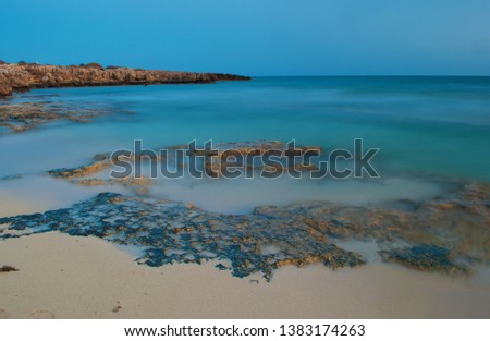 View of empty sandy barren Poseidon Beach near ayia napa, Cyrpus. Blue sky above shallow water with reefs. Warm evening in fall. Copy space. Long exposure