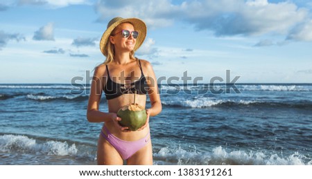 A girl in a hat and swimsuit is standing on the beach and holding a coconut. Banner Panorama