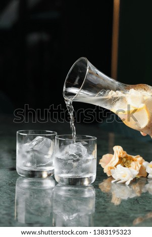 water with lemon pours from a glass decanter into old-fashioned glasses with ice on a green marble table on a black background