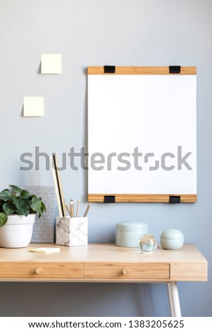 Stylish scandinavian interior with wooden design desk, mock up poster frame, elegant office accessories, memo stick on the wall and beautiful plant. Cozy home decor. Gray background wall. Real photo.