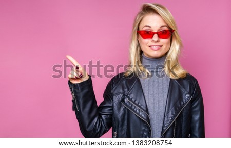 Photo of blonde in pink glasses and leather jacket pointing finger to side