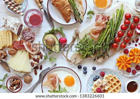  Brunch or breakfast table, meal variety with fried egg, asparagus, avocado, sausage and cheese variety, croissants, smoothie, fresh waffles and fruits. Overhead view