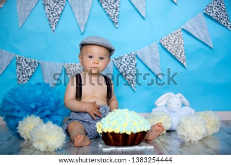 Little baby boy, celebrating his first birthday with smash cake party, studio isolated shot on blue background