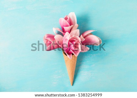 Ice cream cone with pink magnolia flowers bouquet on blue background. Minimal spring concept. Flat lay. top view. wedding background