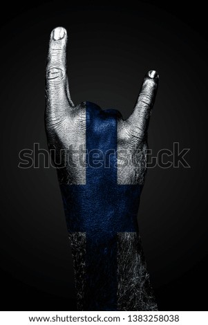 A hand with a drawn Finland flag shows a goat sign, a symbol of mainstream, metal and rock music, on a dark background. Vertical frame