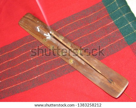 An incense stick burning in a holder on a red cloth background 