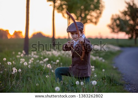 Portrait of child playing with bow and arrows, archery shoots a bow at the target on sunset Royalty-Free Stock Photo #1383262802