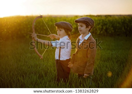 Portrait of child playing with bow and arrows, archery shoots a bow at the target on sunset Royalty-Free Stock Photo #1383262829