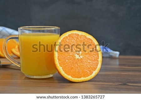 A glass of orange juice stands on a wooden surface, next to it is half an orange and pieces of orange peeled on the surface - concept with space for text or other elements