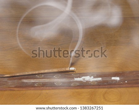 A burning incense stick with streams and trails of smoke in the air 
