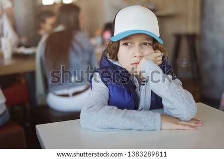 Cute little boy sitting at the table in a white tracker hat. Horizontal mock up.