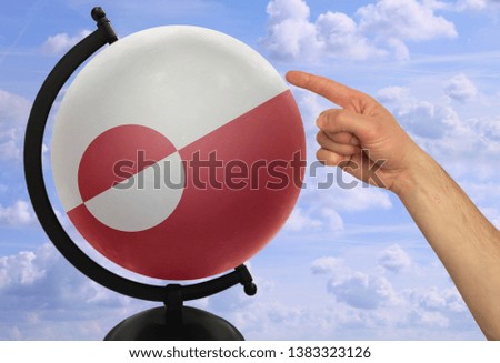 The index finger of a male hand points to a globe with a colored flag greenland