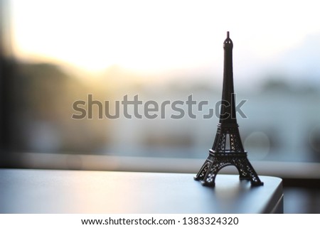 Eiffel tower miniature upon table with sunset to the background - paris tower in office with sunrise - paris tower with sunrise to the background - whit space text or caption

