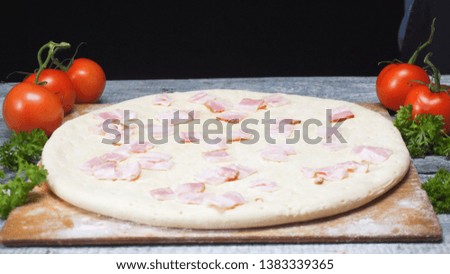 Close-up of chef in protective gloves making Italian pizza and adding the pieces of ham or bacon on the pizza dough. Frame. Pizza preparation and ingredients