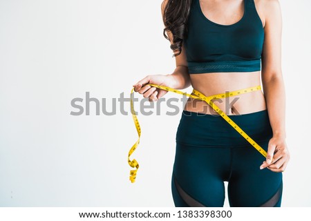 Close up shot of woman with slim body measuring her waistline and torso. Healthy nutrition and weight losing concept. Royalty-Free Stock Photo #1383398300