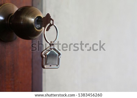 House key with home keyring in keyhole on wood door, copy space