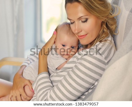 Portrait of mother and her 2-month-old child. Blonde hair, striped clothes.