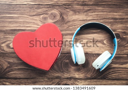 White headphones and red heart gift box on wooden background.