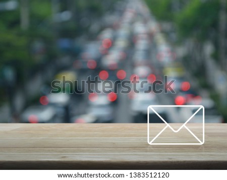 email flat icon on wooden table over blur of rush hour road with cars in city, Contact us concept