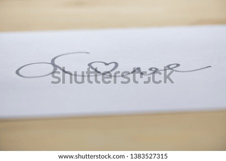 Hand writing " Love " on white paper texture, Wooden table background, Close up shot, Selective focus, Stationery concept
