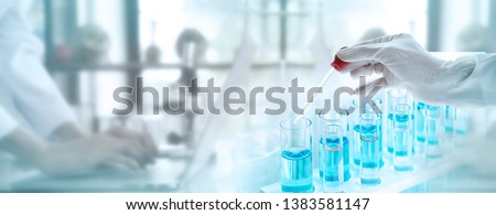 Test tubes with liquid in laboratory, Doctor hand holding dropper with dripping transparent glass pipette. scientist working with laptop background for banner size text space. Royalty-Free Stock Photo #1383581147