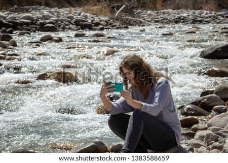 Young beautiful girl on nature takes a selfie on the phone and takes pictures of nature. Good mood on a bright spring day. Tourism and travel.
