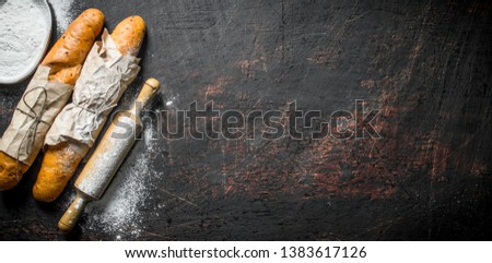 Fresh French baguette with flour and rolling pin. On dark rustic background