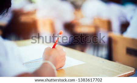 Hand of students writing and taking exam with stress in classroom.