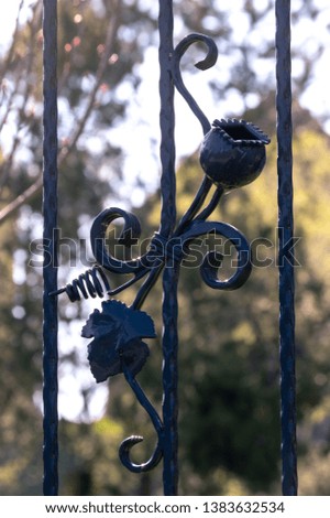 metal fence ornament depicting a poppy capsule and vine leaf